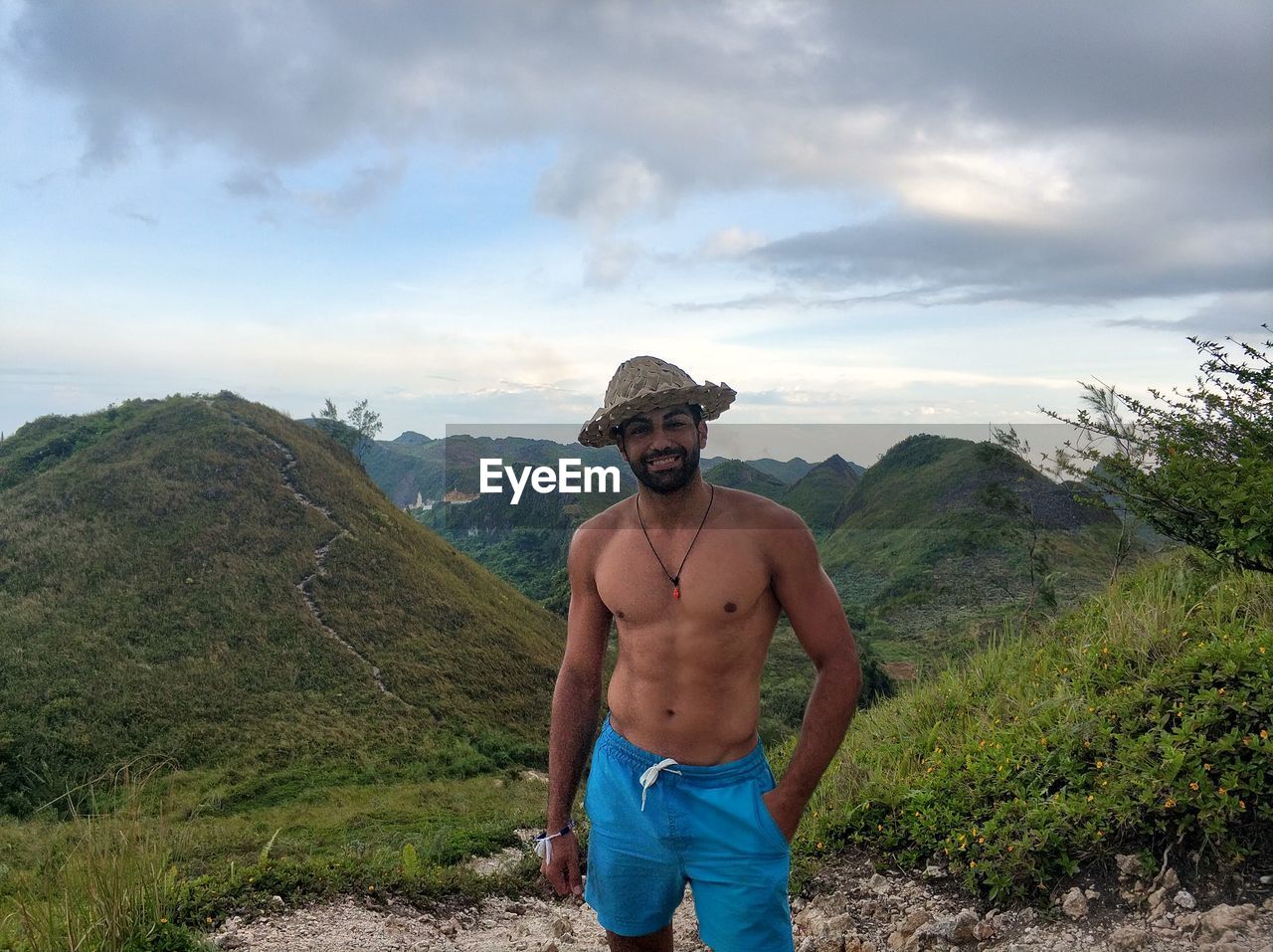 Portrait of shirtless young man standing against mountains