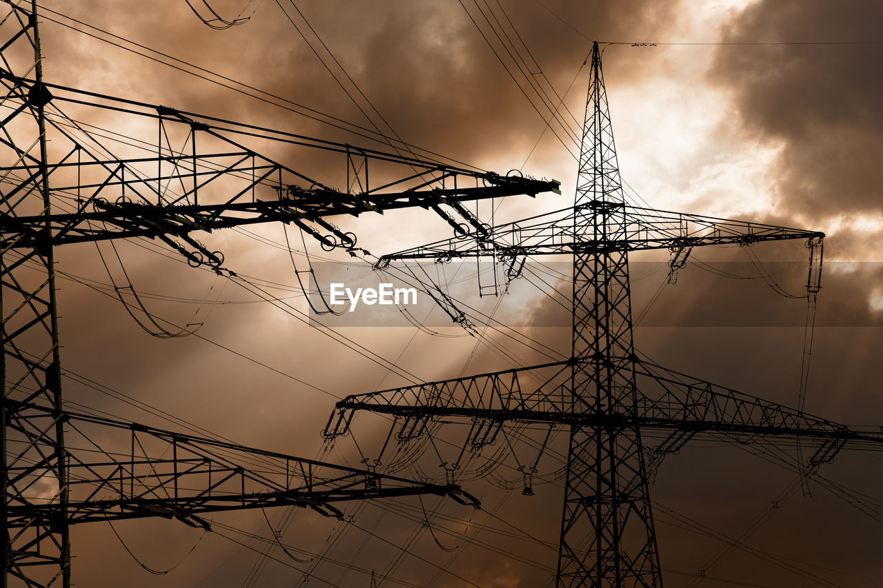 Low angle view of electricity pylon against cloudy sky