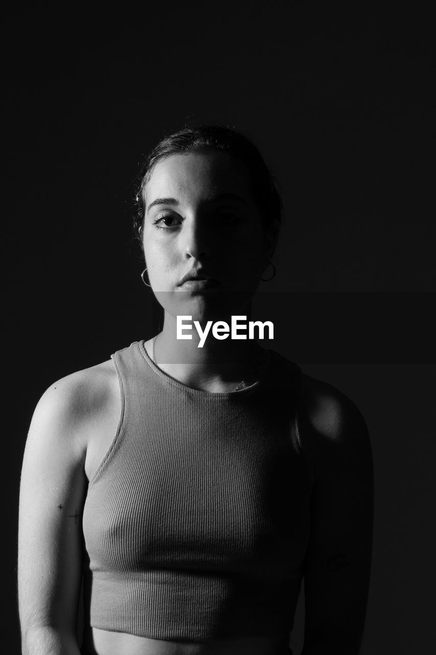 Portrait of young woman standing against black background