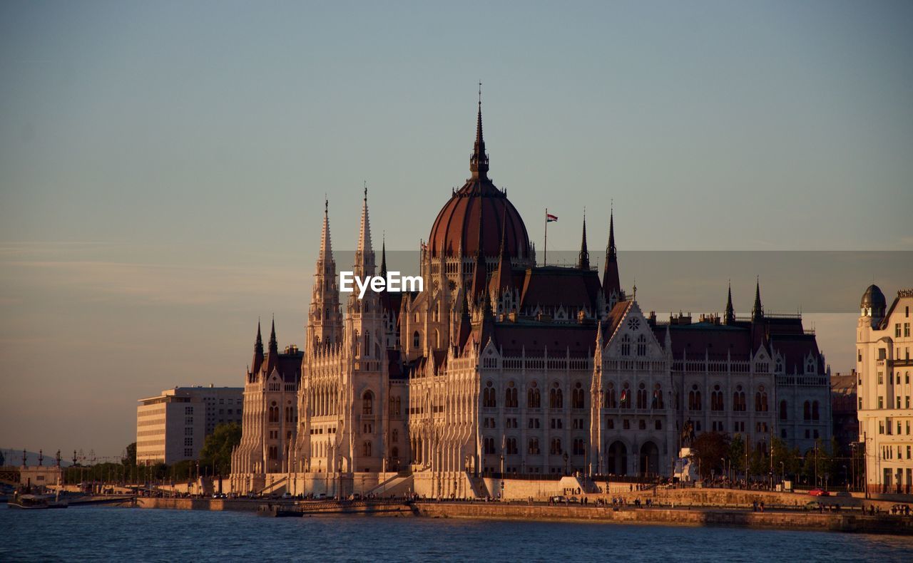 Hungarian parliament building by river danube against sky at morning
