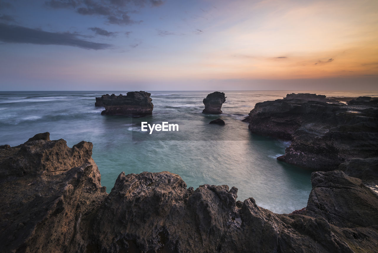 Rocks on sea against sky during sunset