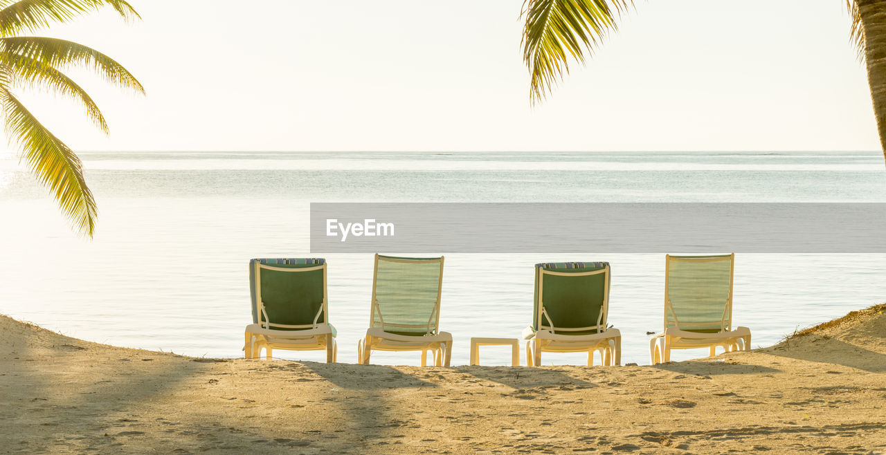 EMPTY CHAIRS ON BEACH AGAINST SKY