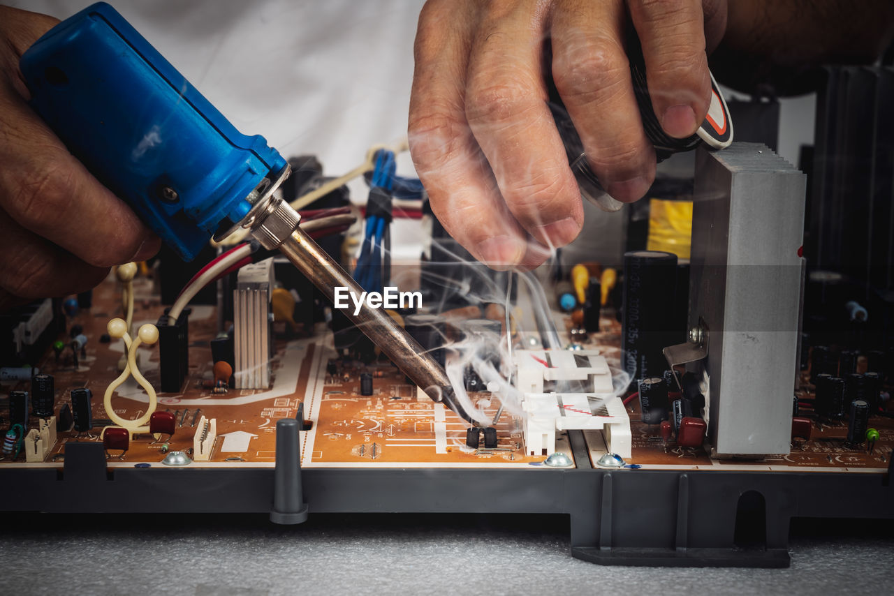 A technician is repairing a circuit board, by using a soldering iron and lead coils