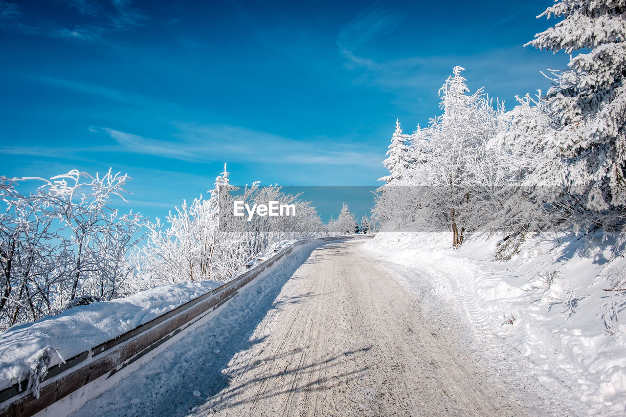 Snow covered road by trees against blue sky