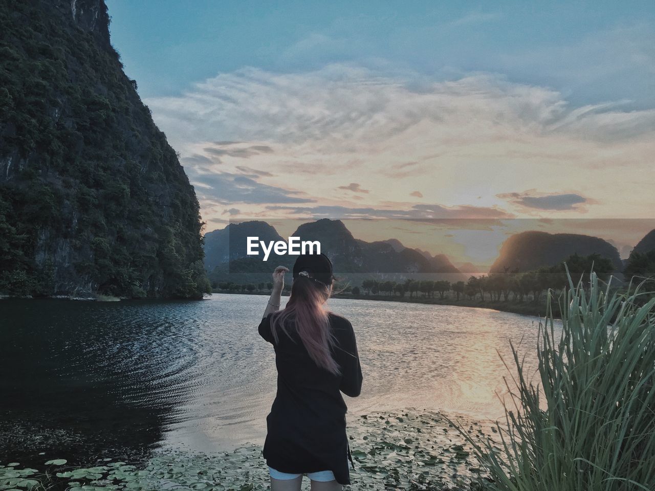 Rear view of woman looking at lake during sunset