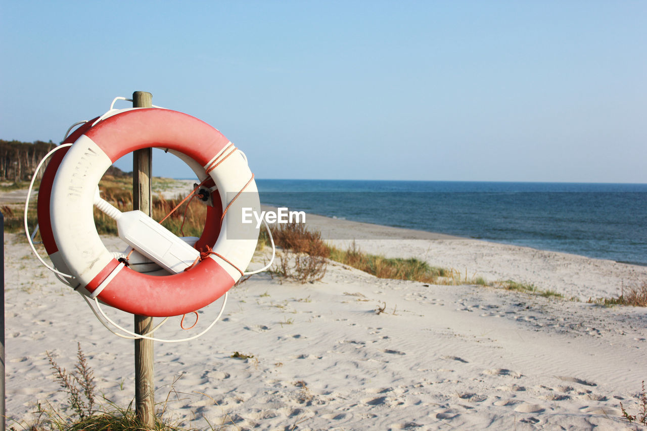 Inflatable ring on wooden post at beach against sky