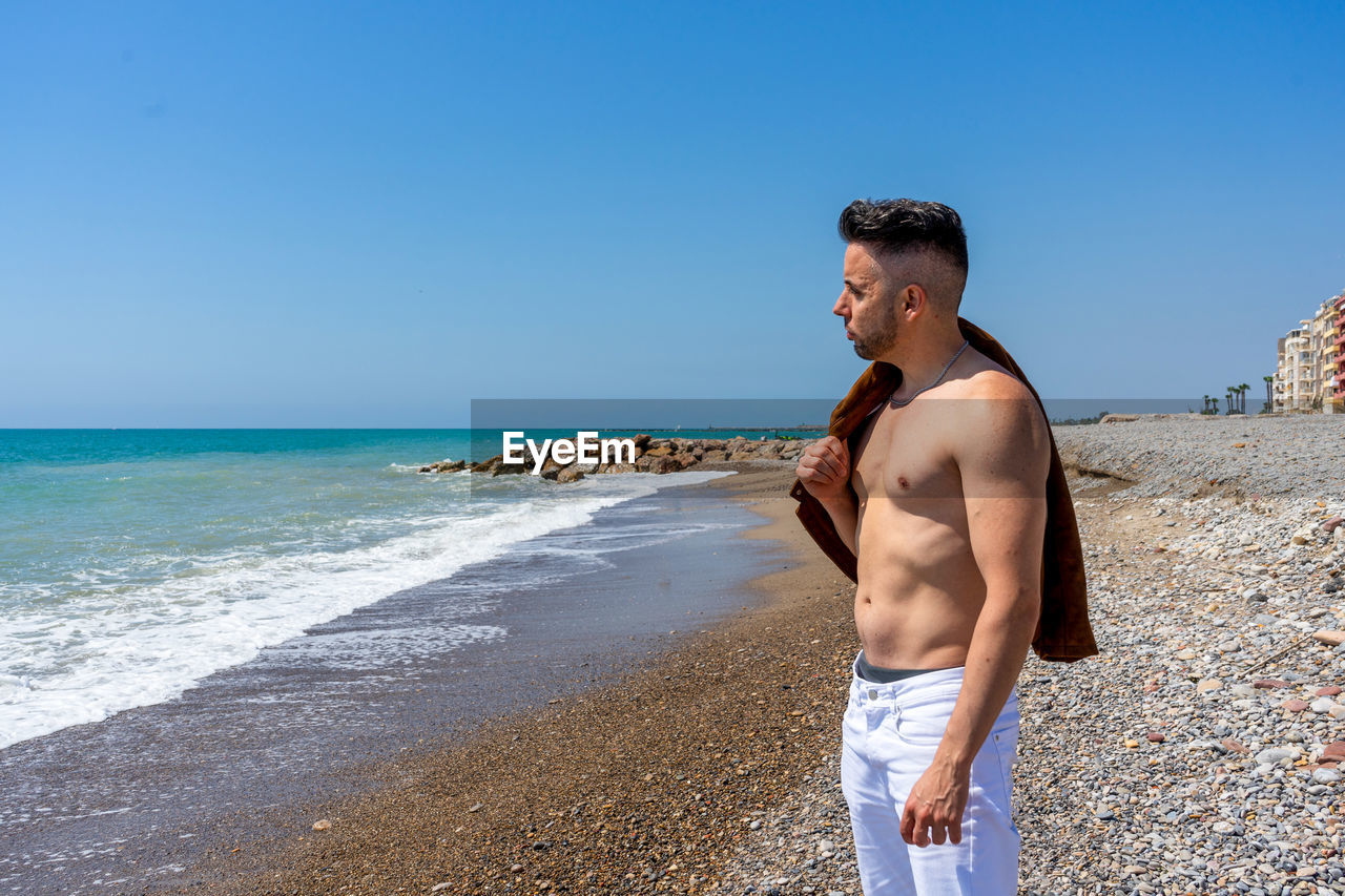 Man standing at beach against clear blue sky