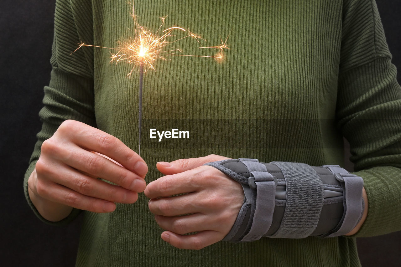 Midsection of woman holding illuminated sparkler with bandage on hand