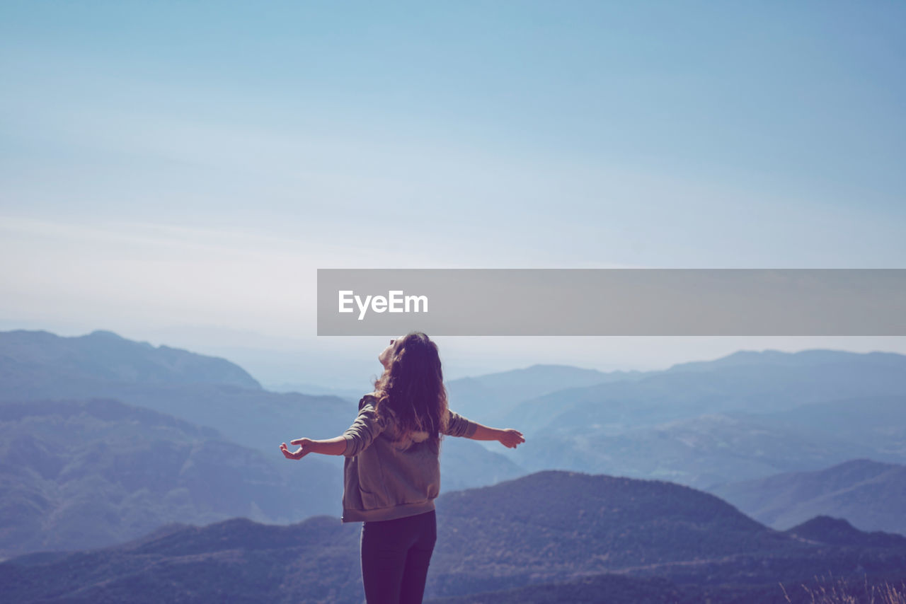 Rear view of woman standing on mountain against sky