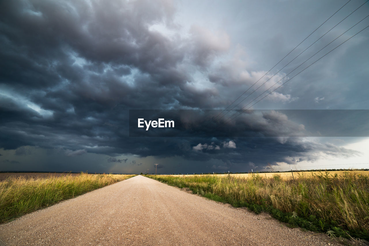 Empty road amidst landscape against cloudy sky