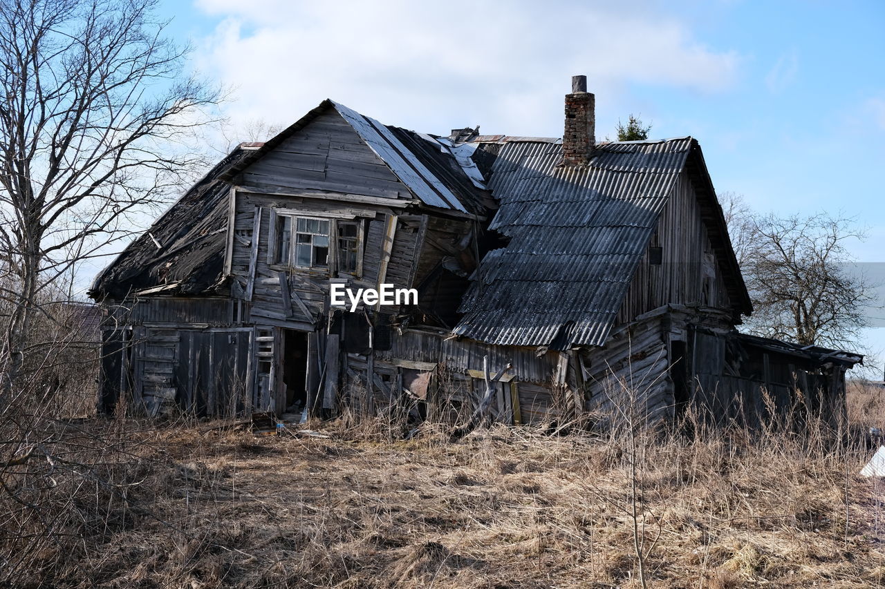 EXTERIOR OF OLD HOUSE ON FIELD BY BUILDING AGAINST SKY