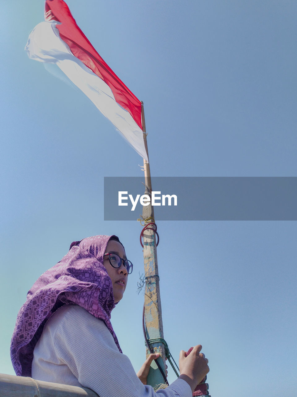 Low angle view of woman standing with indonesian flag against clear blue sky