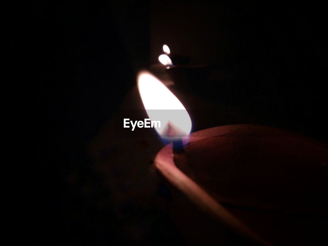 CLOSE-UP OF HUMAN HAND HOLDING LIT CANDLE IN DARKROOM