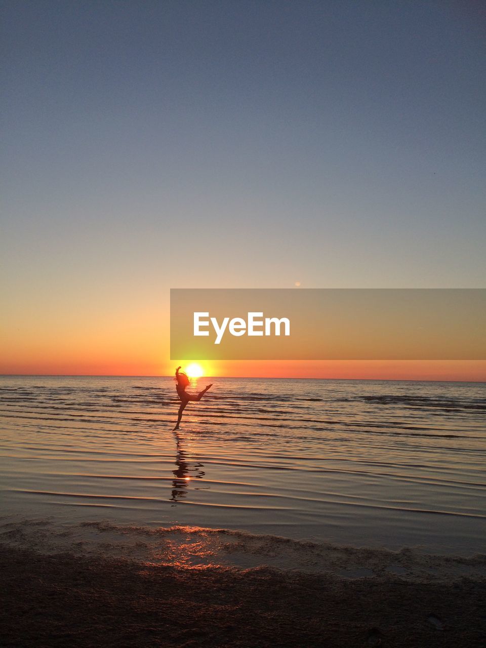 Silhouette woman jumping on shore at beach against clear sky during sunset