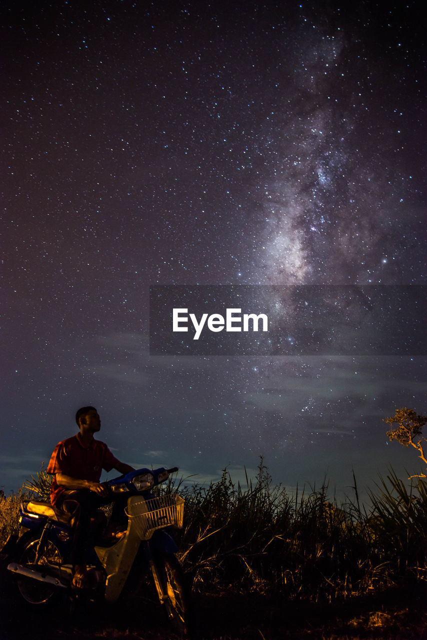 Man riding motor scooter on field against star field