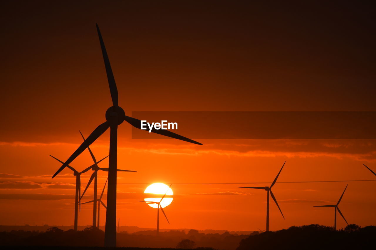 A bright red sunset through wind turbines