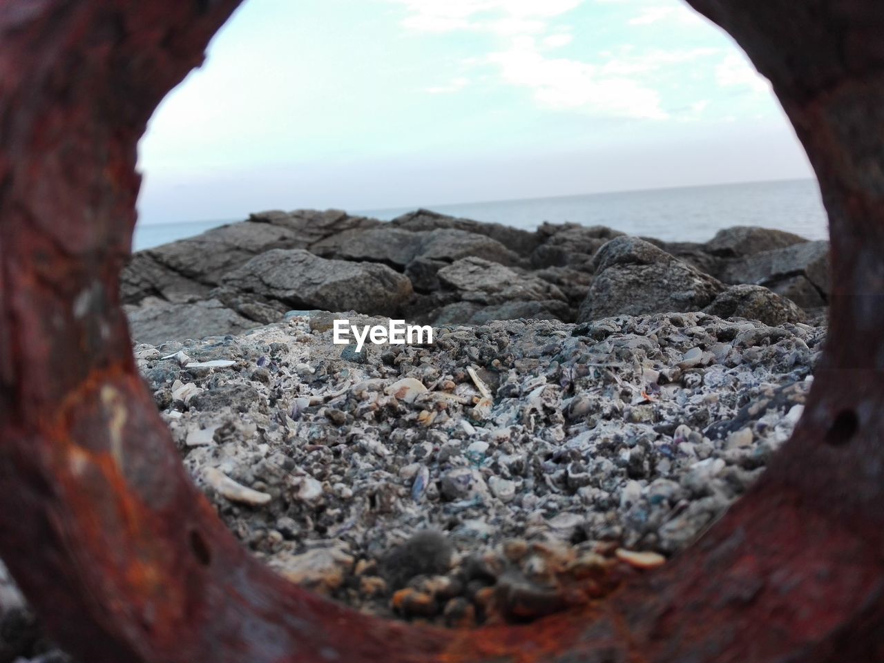 Rocky shore at sea against sky seen through rusty metal