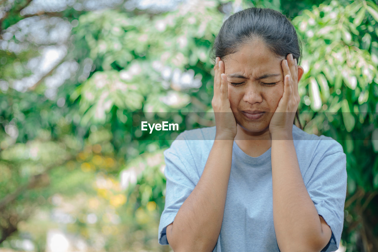 Woman touching head in pain against trees