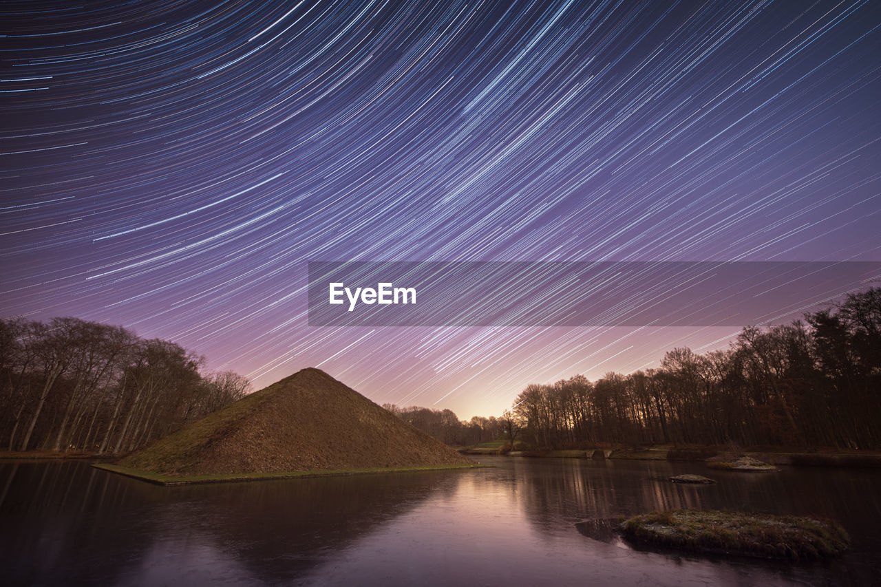 Scenic view of lake against star trails in sky at night