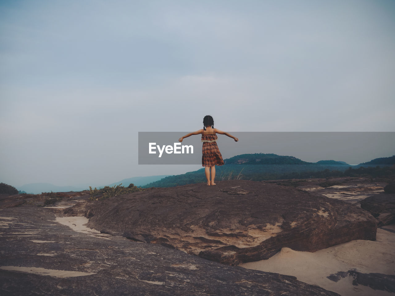 Rear view of girl standing on rock against sky