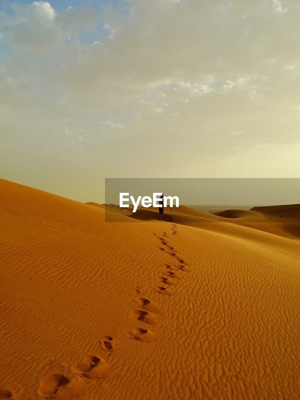 Mid distance view of people on sand dunes at desert against sky during sunset