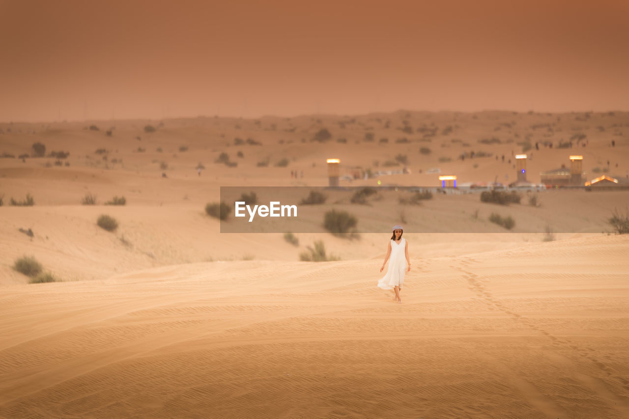 Young woman walking on desert against sky during sunset
