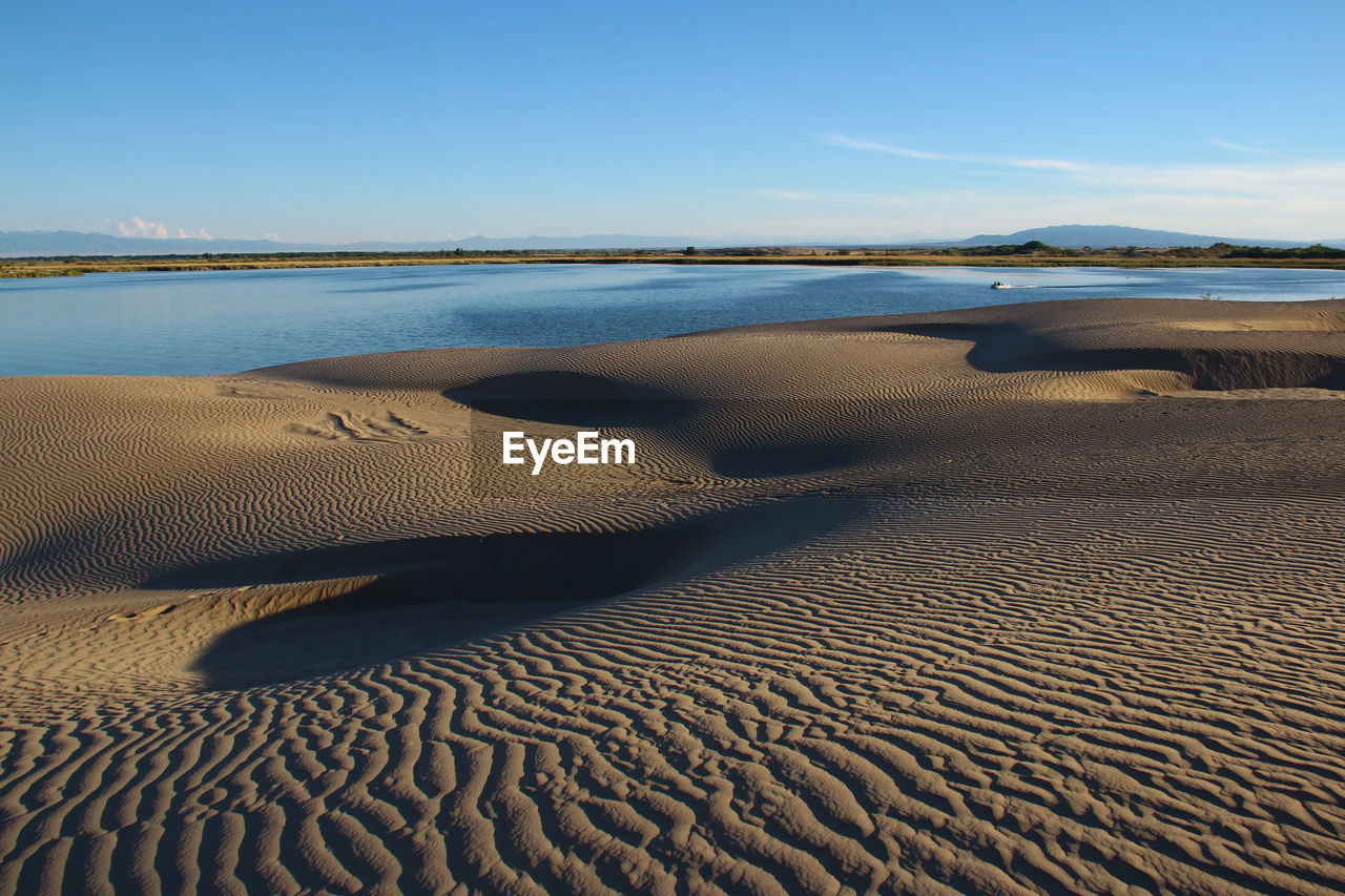 Lake with sand dunes against a blue sky in summer, sunny day