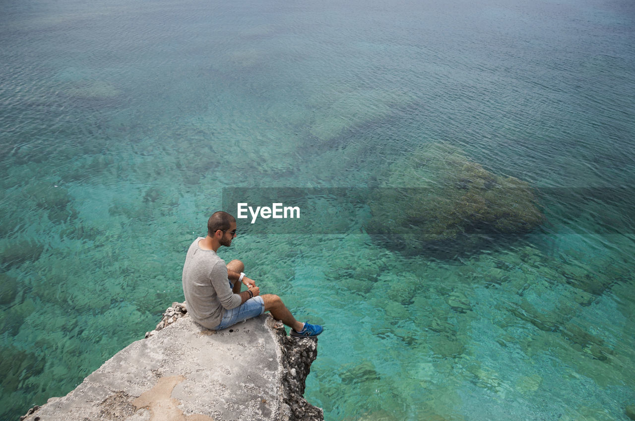 High angle view of mid adult man looking at sea while sitting on rock