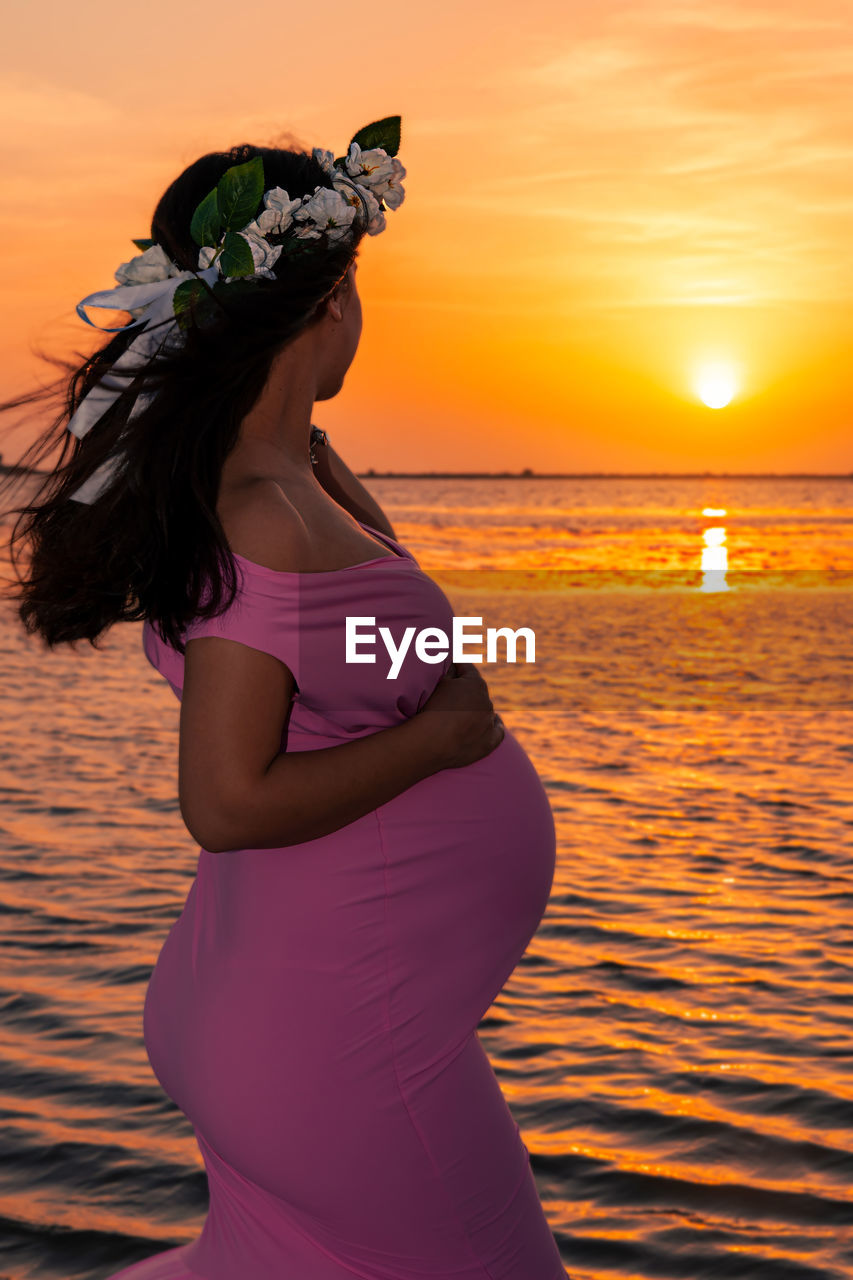 WOMAN STANDING ON SEA SHORE DURING SUNSET