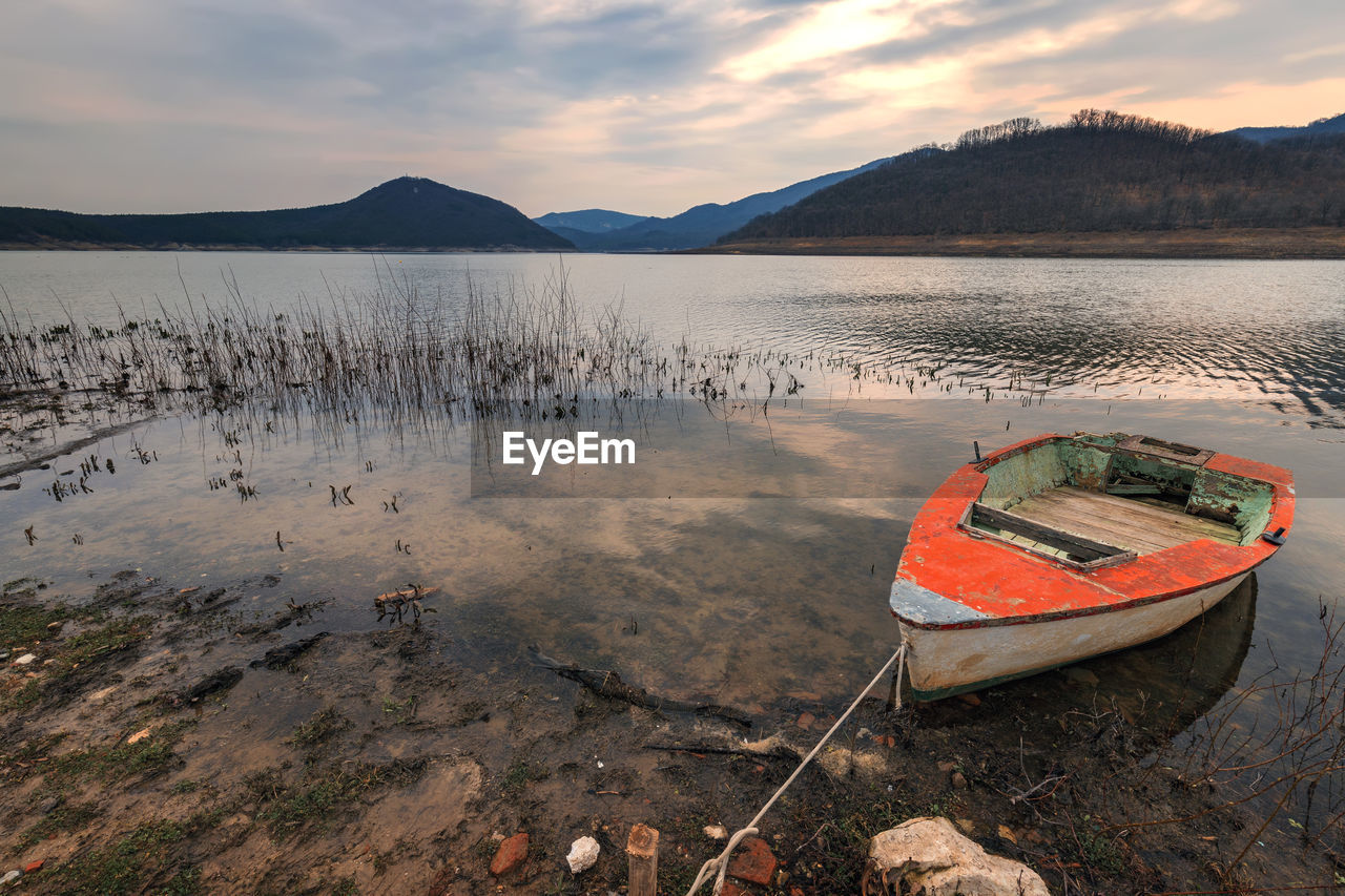 water, sky, reflection, lake, mountain, nautical vessel, nature, scenics - nature, shore, transportation, beauty in nature, boat, tranquility, landscape, beach, cloud, land, tranquil scene, environment, vehicle, mode of transportation, no people, sunset, mountain range, lakeshore, outdoors, moored, travel, non-urban scene, wilderness, travel destinations, coast, day, boating, bay, watercraft