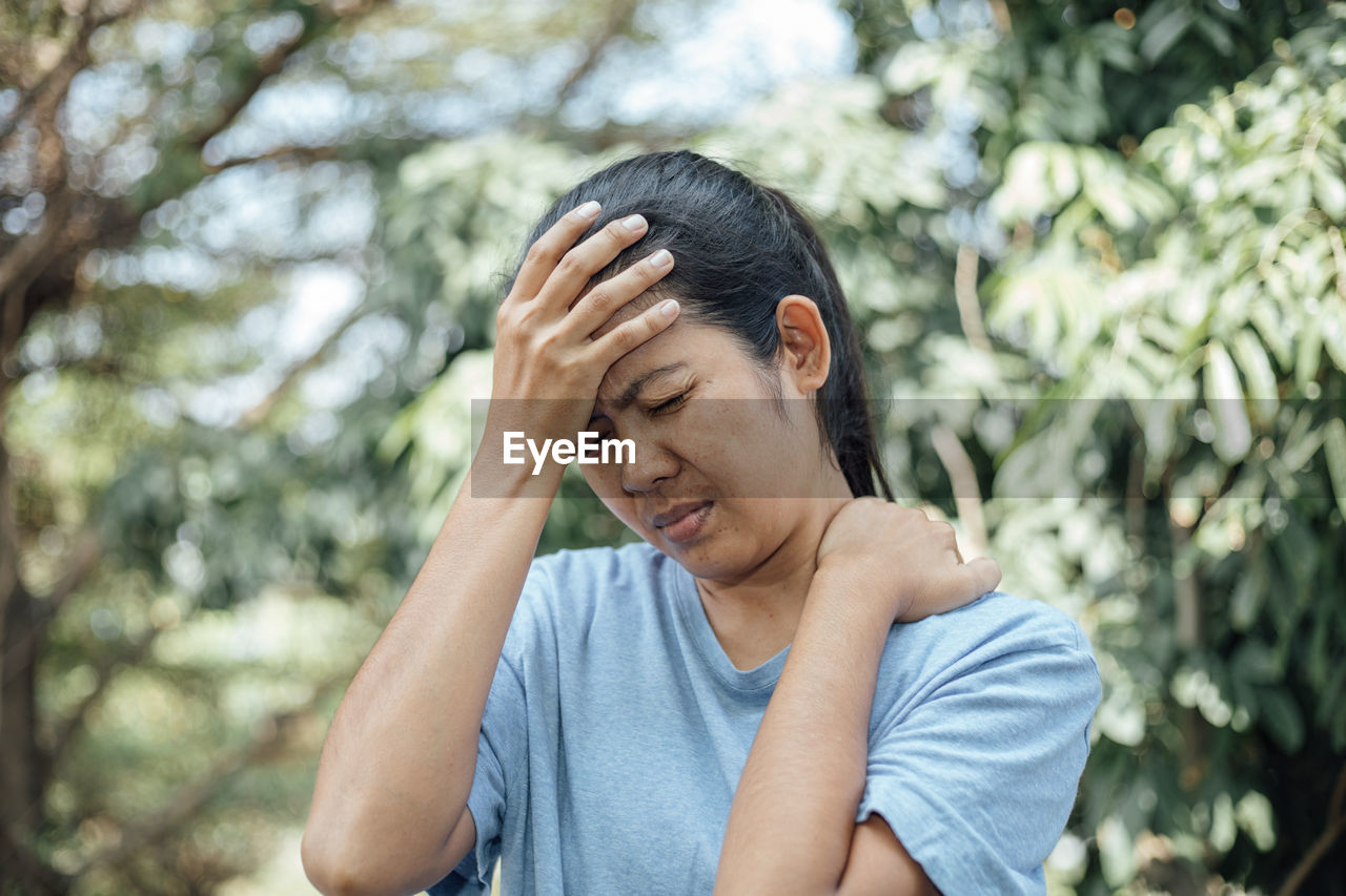 Woman touching head in pain against trees