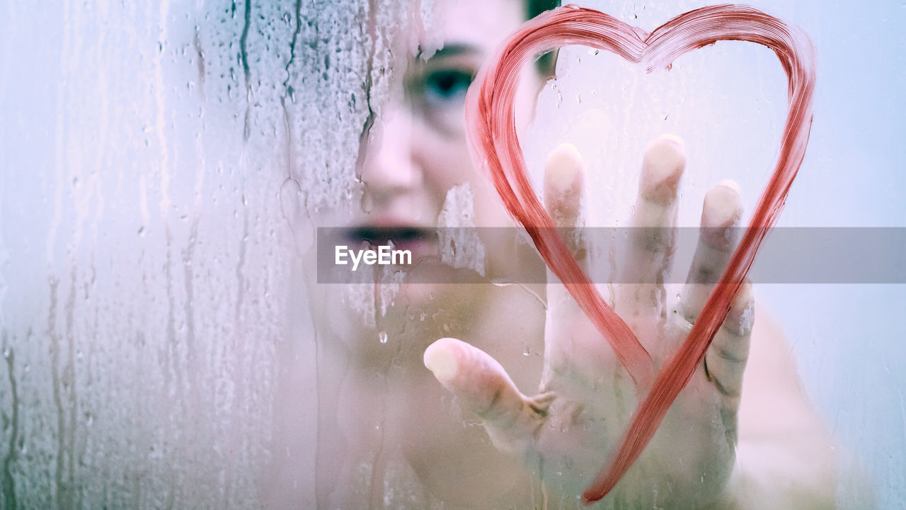 Woman touching heart shape on wet glass