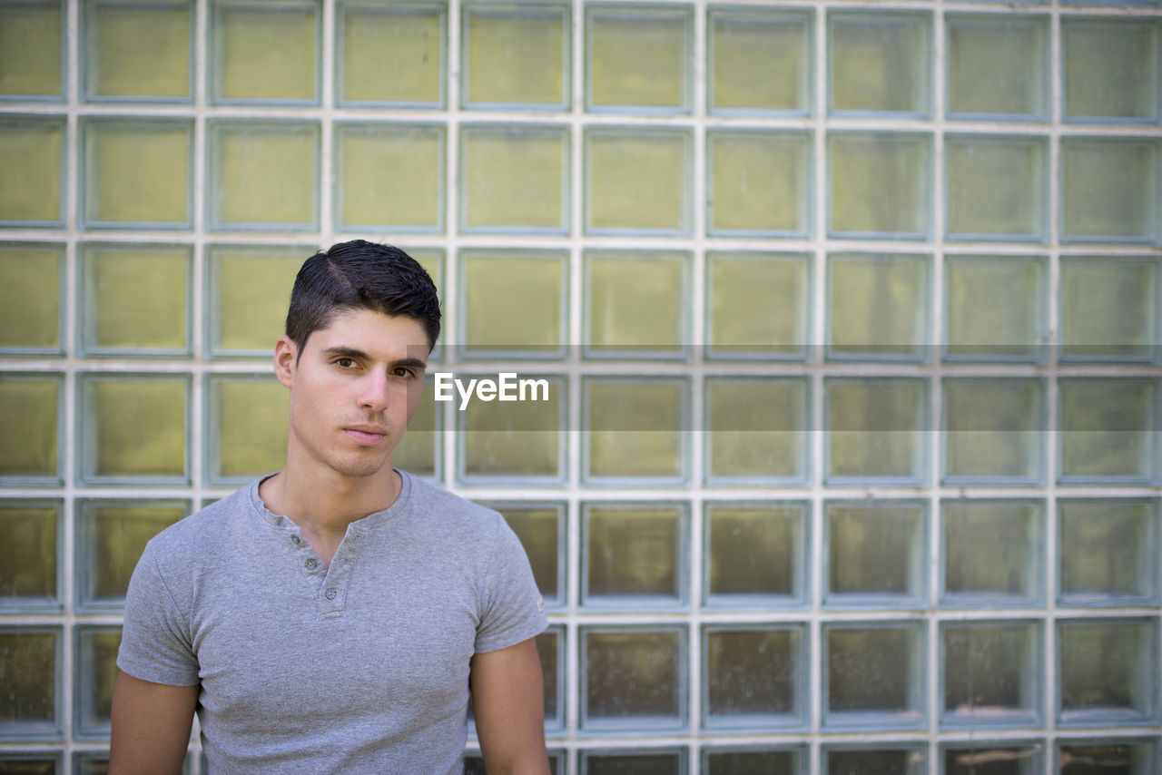 Portrait of young man standing by wall outdoors