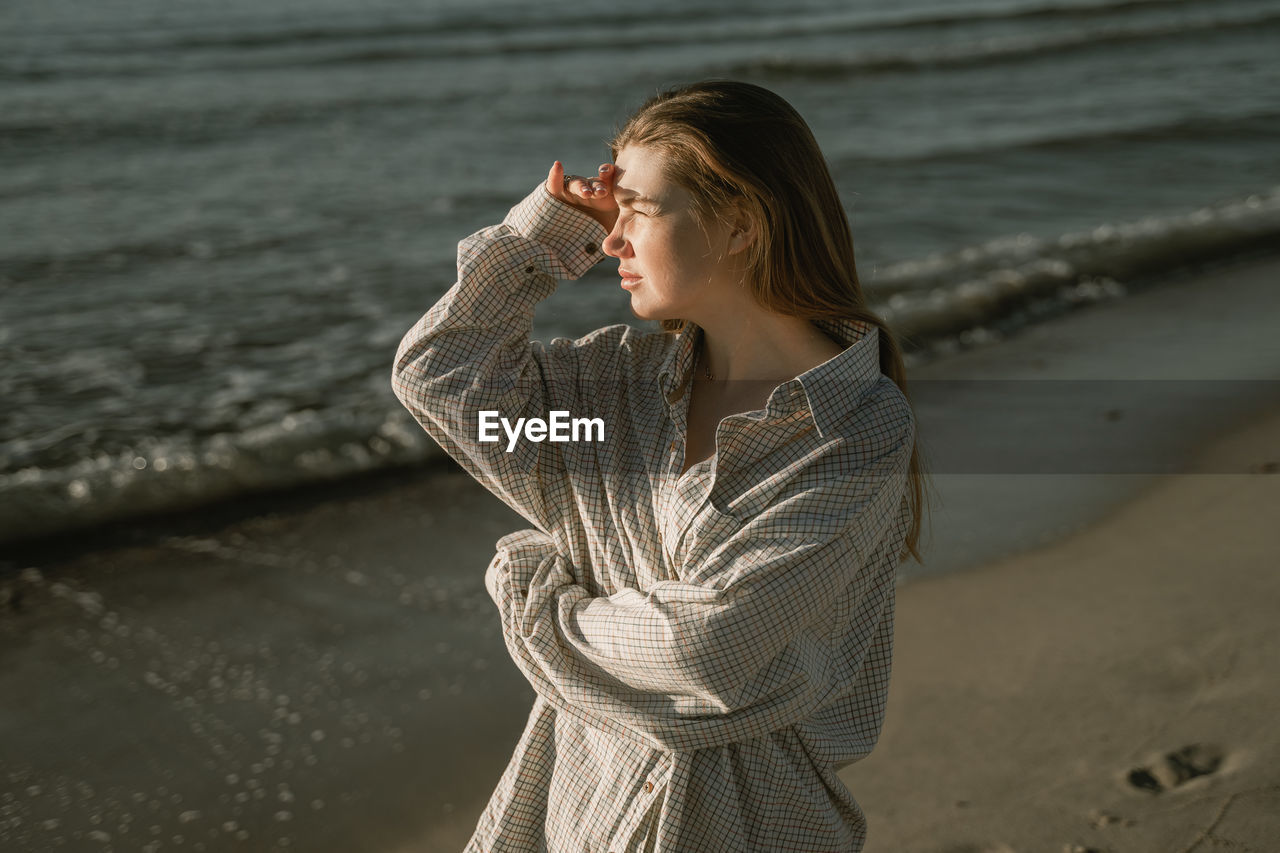 Young woman looking away while standing on beach