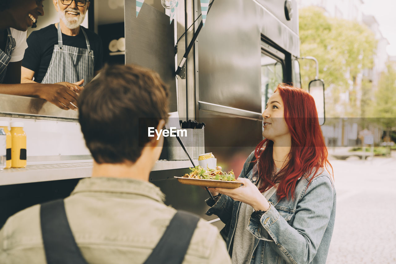 Smiling customer talking to owner while standing with food plate on street