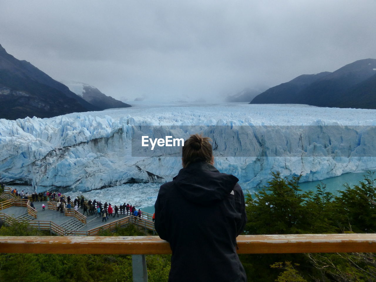 Rear view of mid adult woman looking at snowcapped mountain against cloudy sky