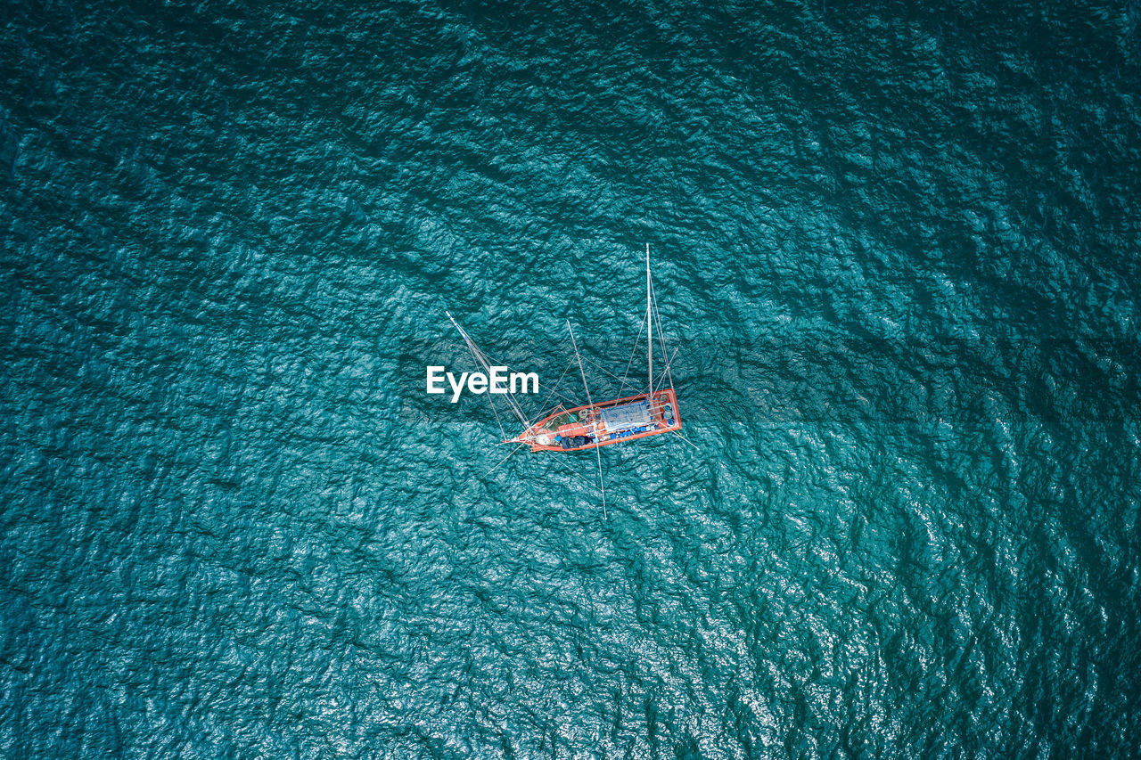 Aerial top view fishing boat sailing on the green sea