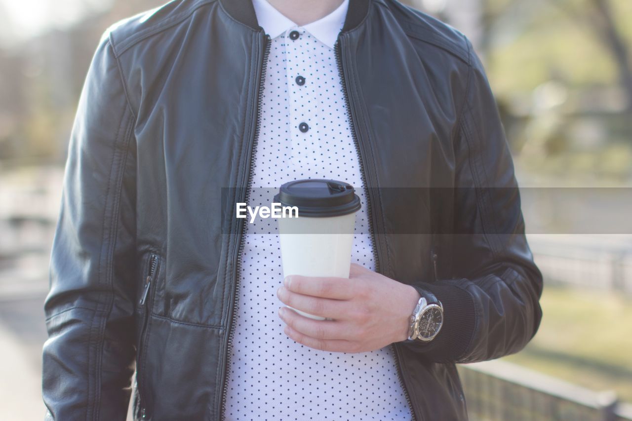 Midsection of man holding coffee in disposable cup