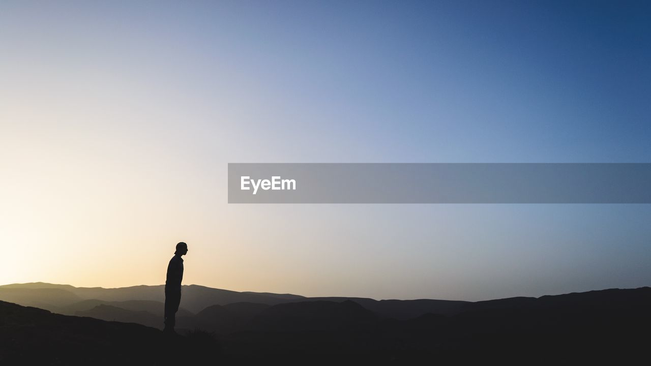 Silhouette man standing on mountain against clear sky