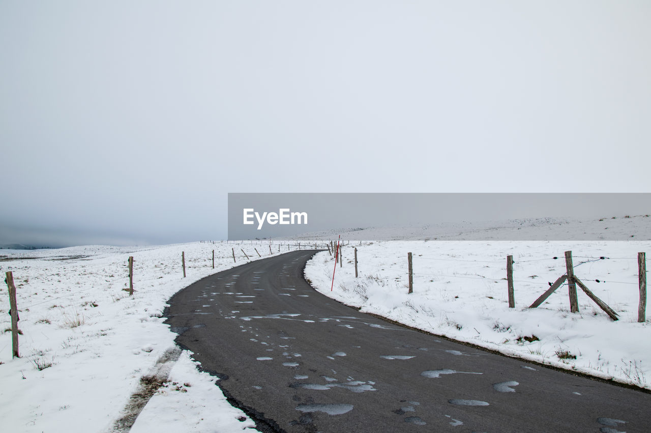 Snow covered road amidst field against sky