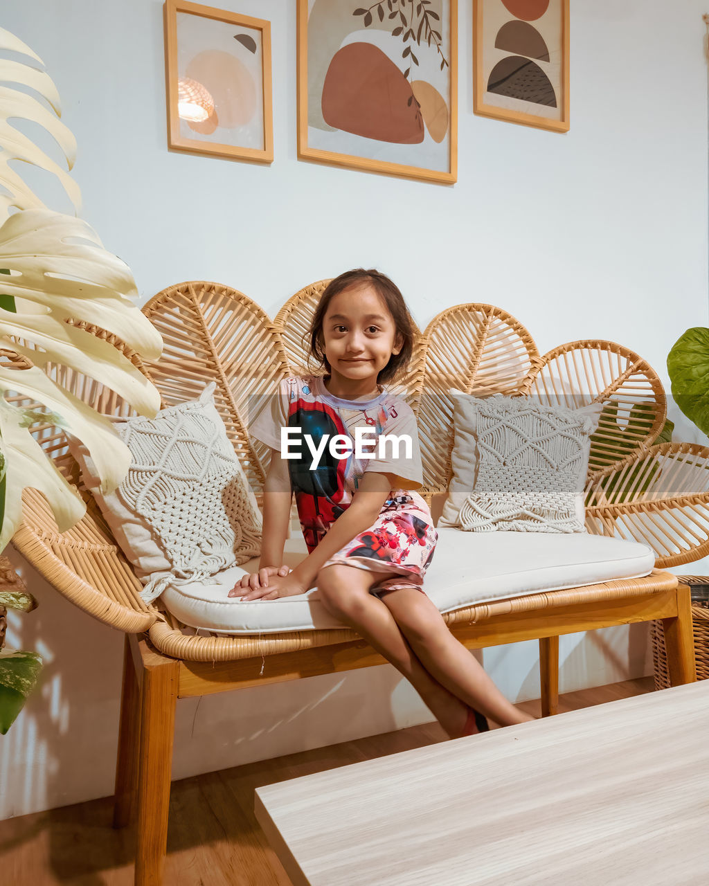 Happy little girl sitting on the rattan couch in a boho interior design.