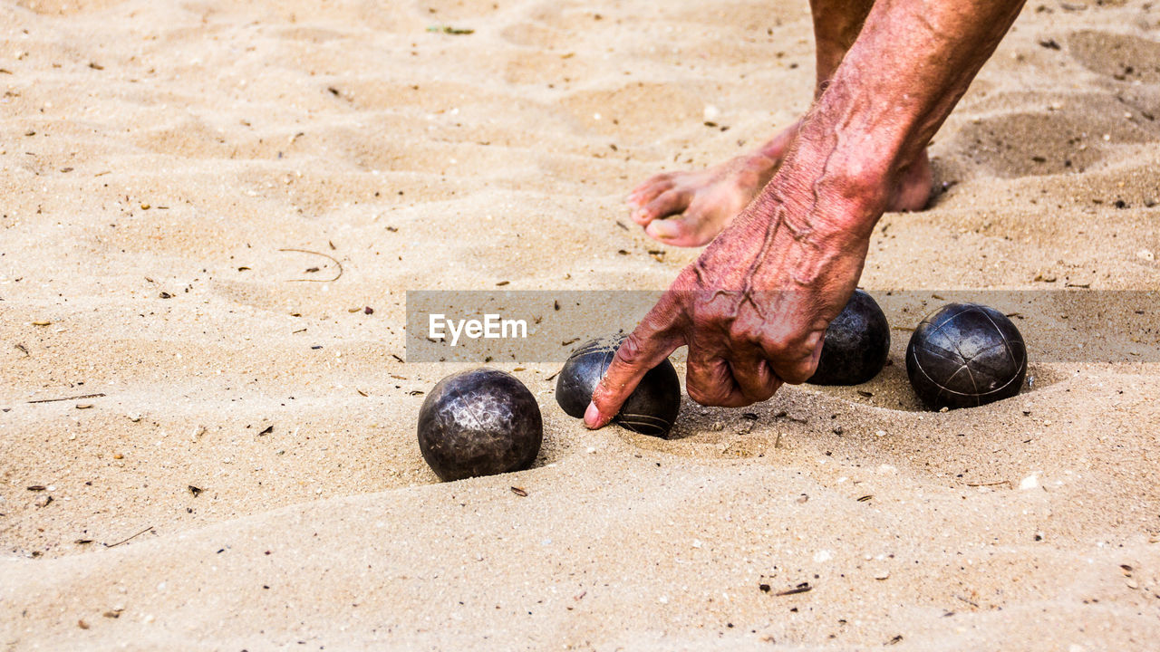 Low section of man playing with balls on sand at beach