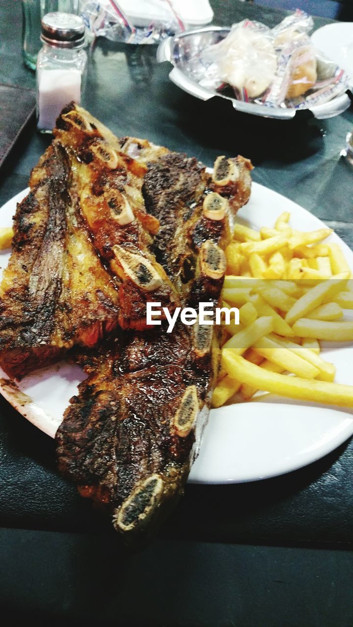 Close-up of grilled meat with french fires served on table