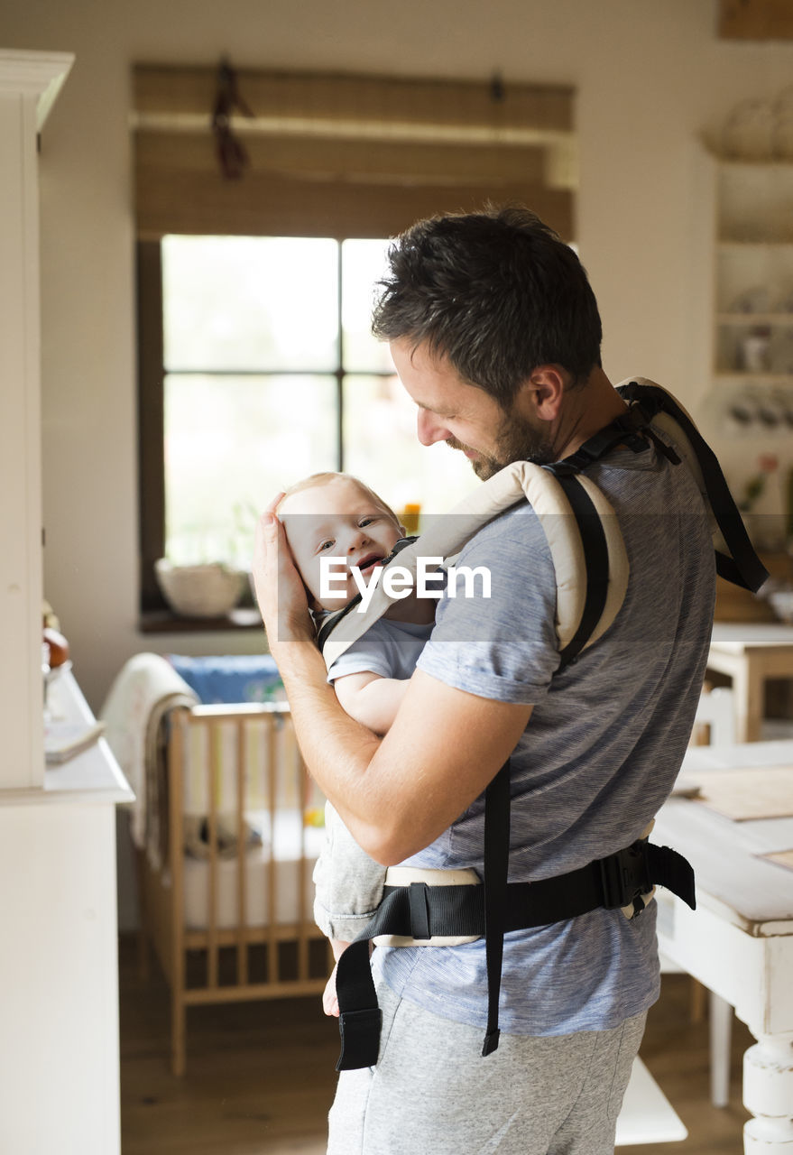 Happy father with baby in baby carrier at home