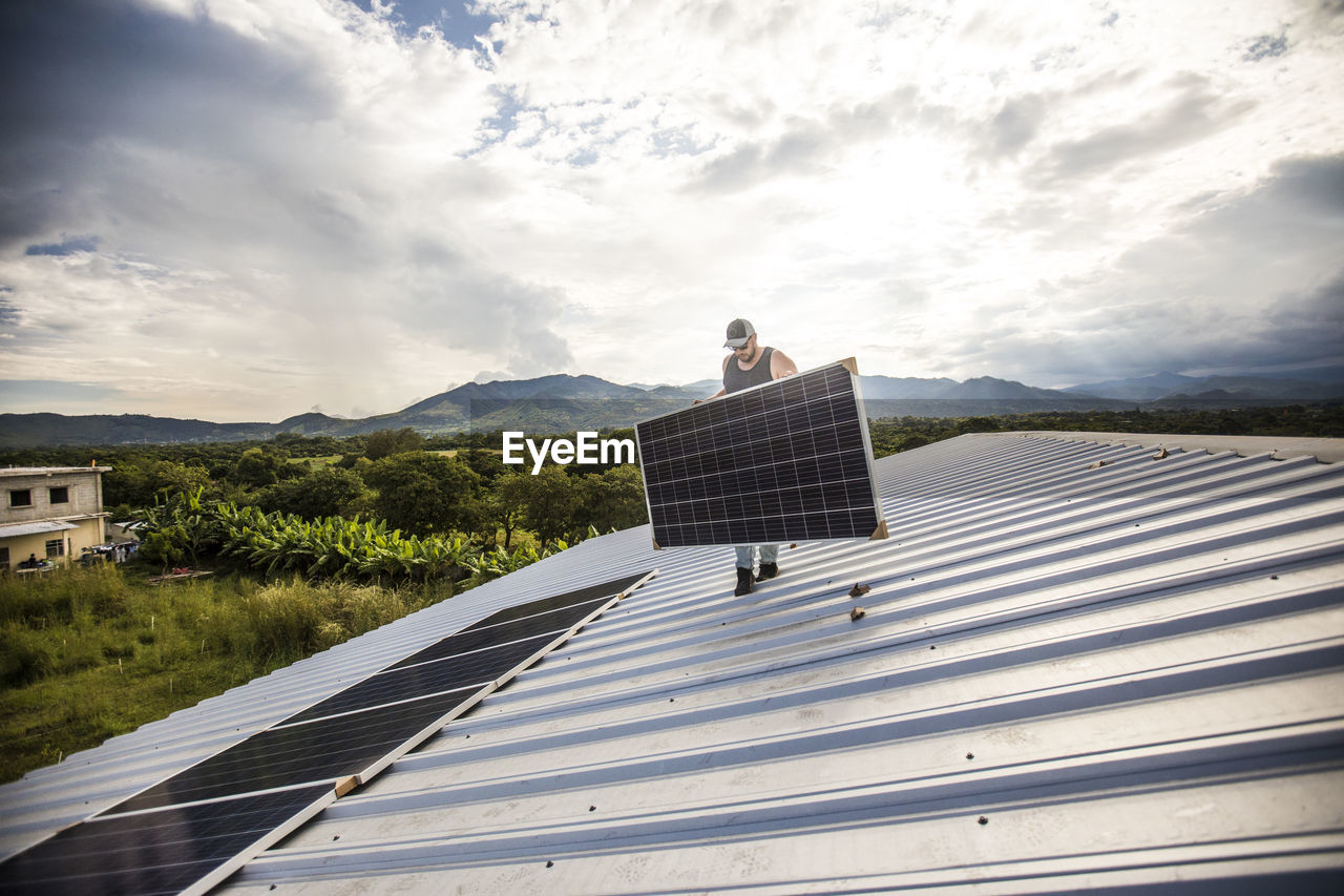 Man carrying solar panel on roof during installation.