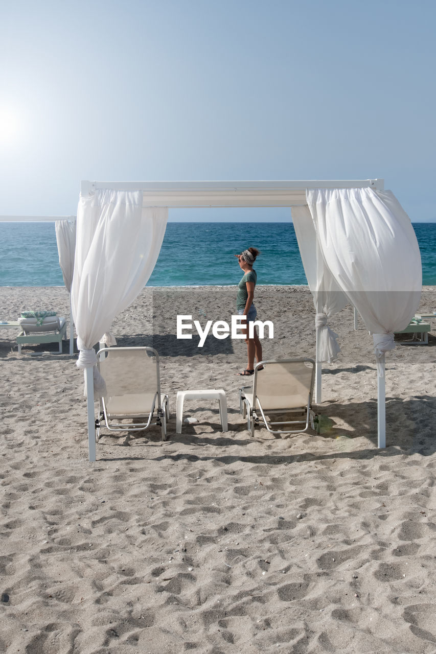 Woman looks at beach with loungers in greece towards the horizon