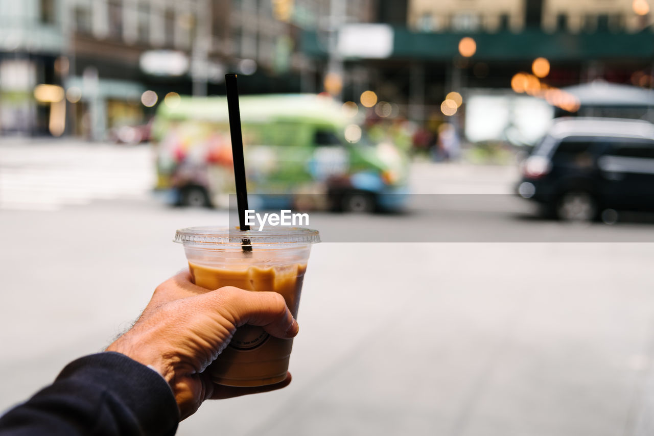 Cropped hand of man holding disposable cup in city