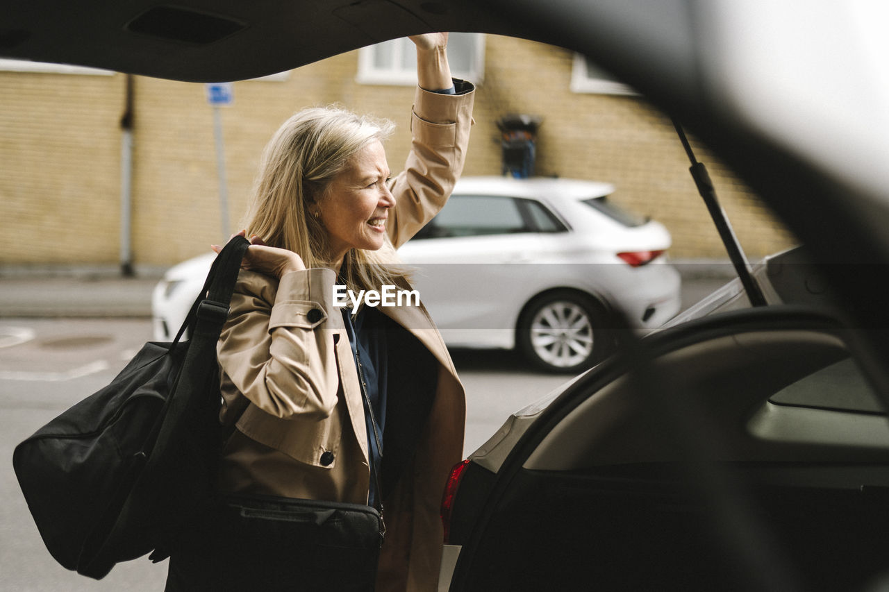 Businesswoman carrying luggage while opening car trunk