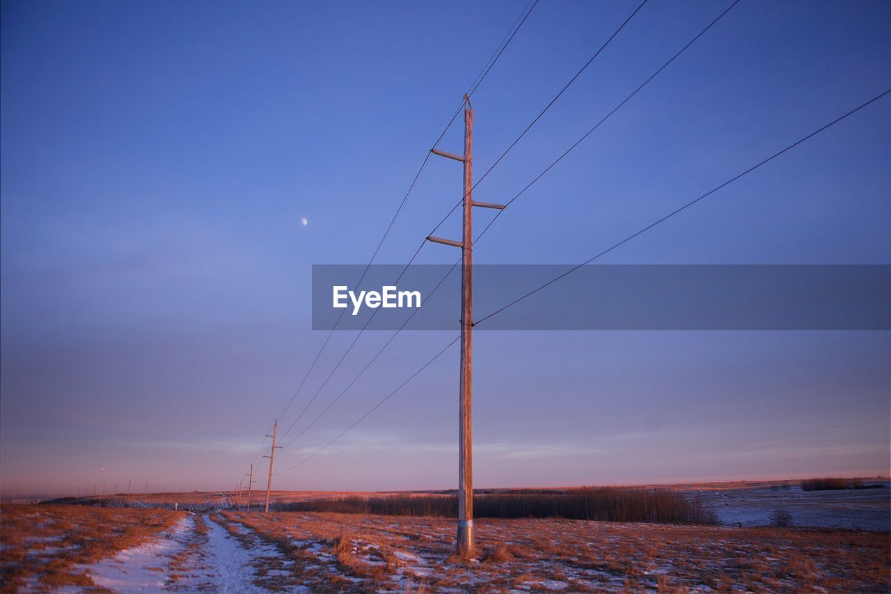 Low angle view of electricity poles on field against sky at dusk