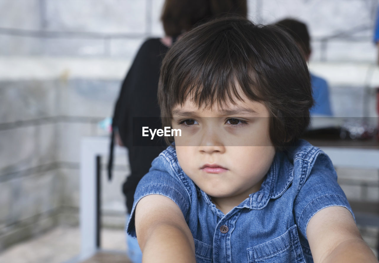 Unhappy toddler boy with sad face, upset boy standing alone looking out with deep in thought